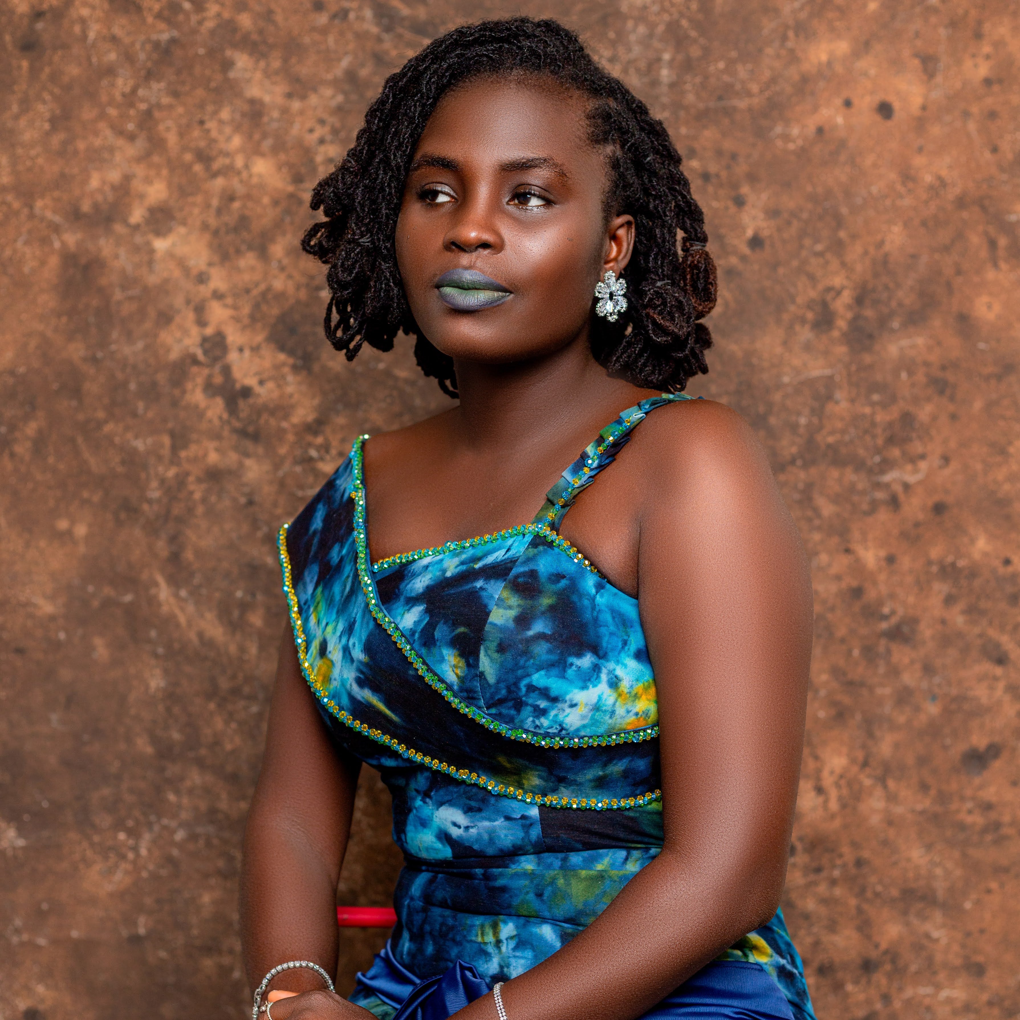 Woman wearing a blue and green Tampoori fabric patterned dress against a brown background
