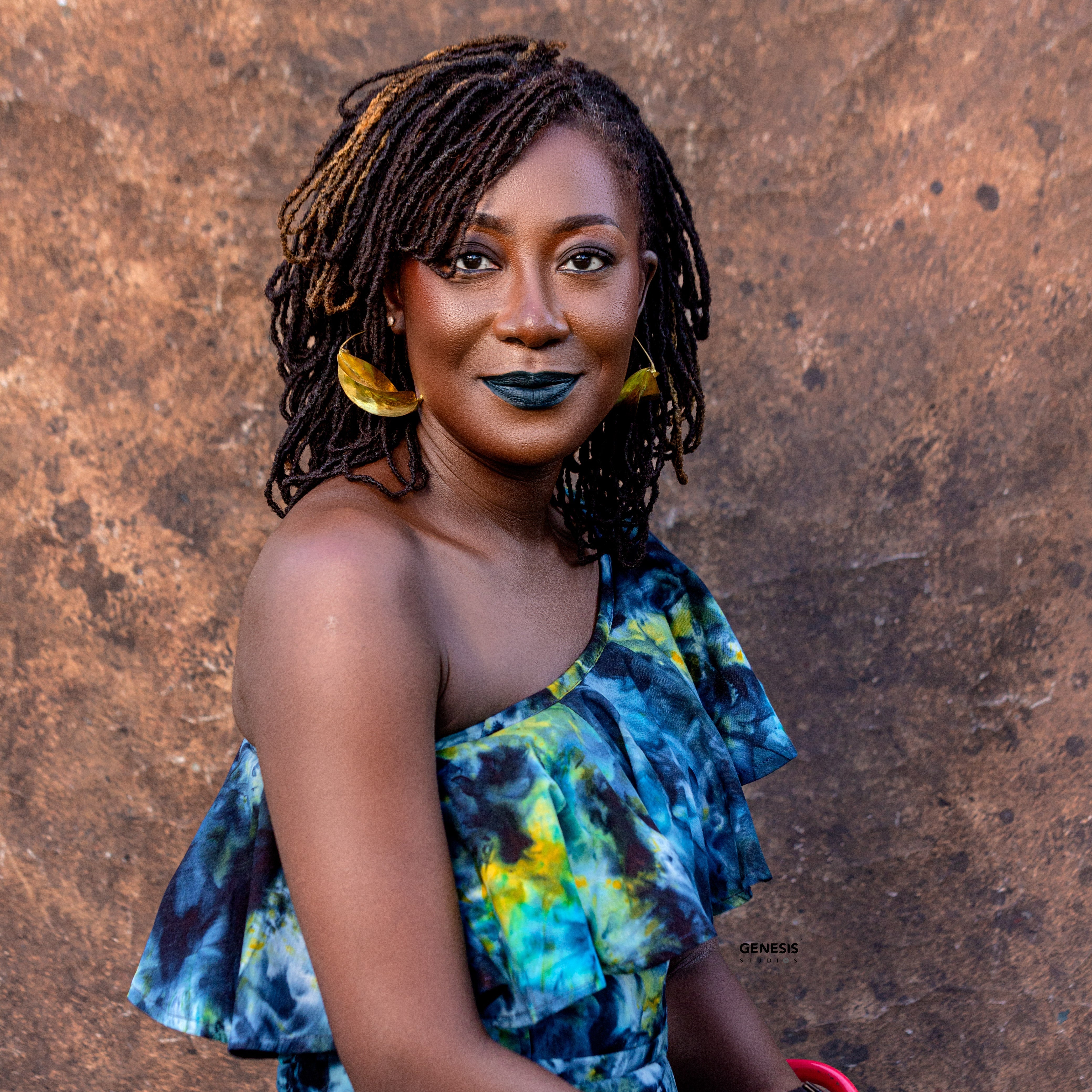 Woman wearing with dark green lipstick wearing a colorful dress made from Tampoori fabric against a textured brown background