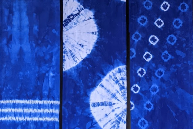 Three blue and white patterned fabrics hanging on a white rack against a gray wall.