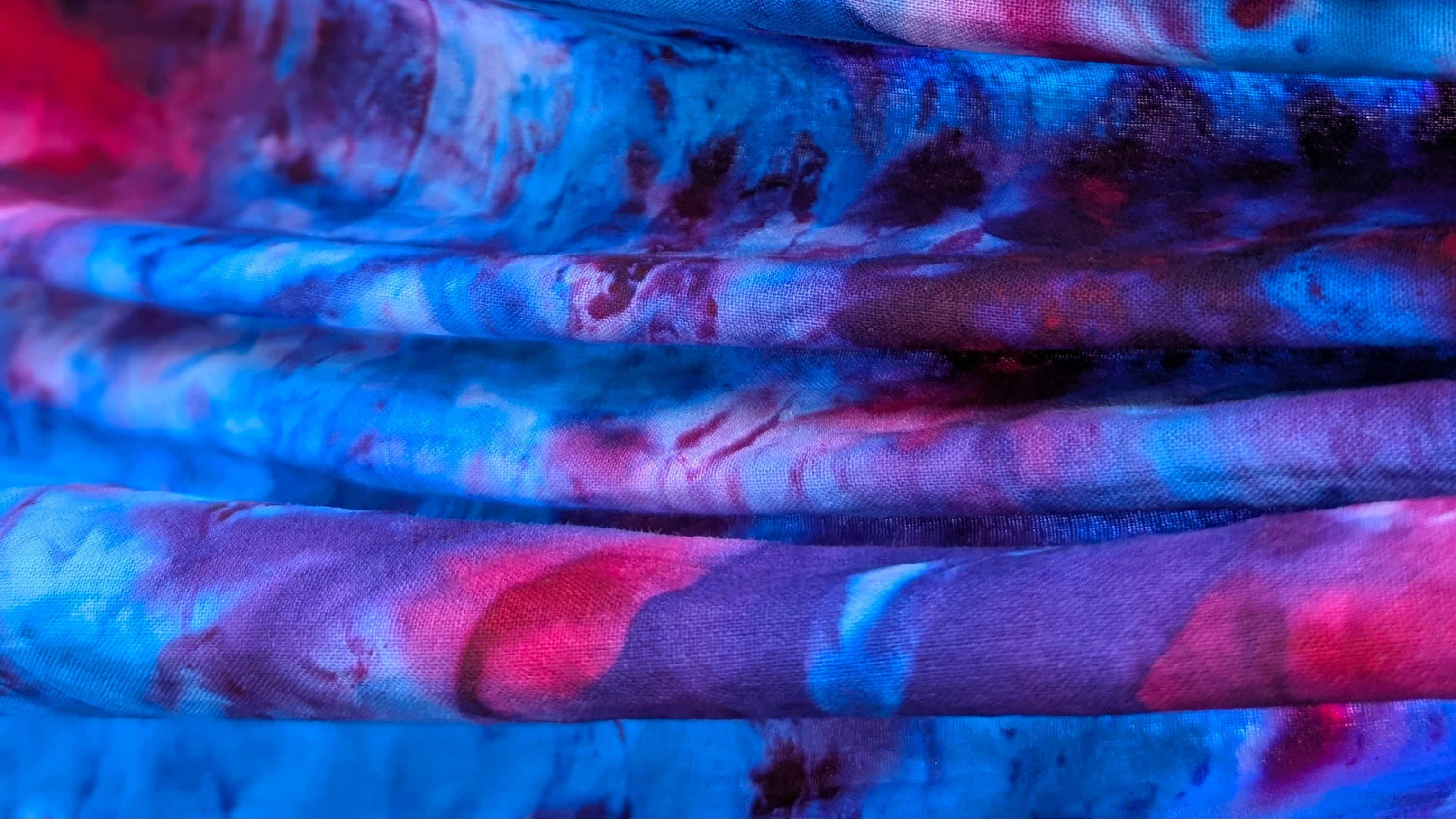 Stack of colorful fabric with a tie-dye handmade in Accra by Tampoori Bubblegum pattern in shades of pink, blue, and purple.