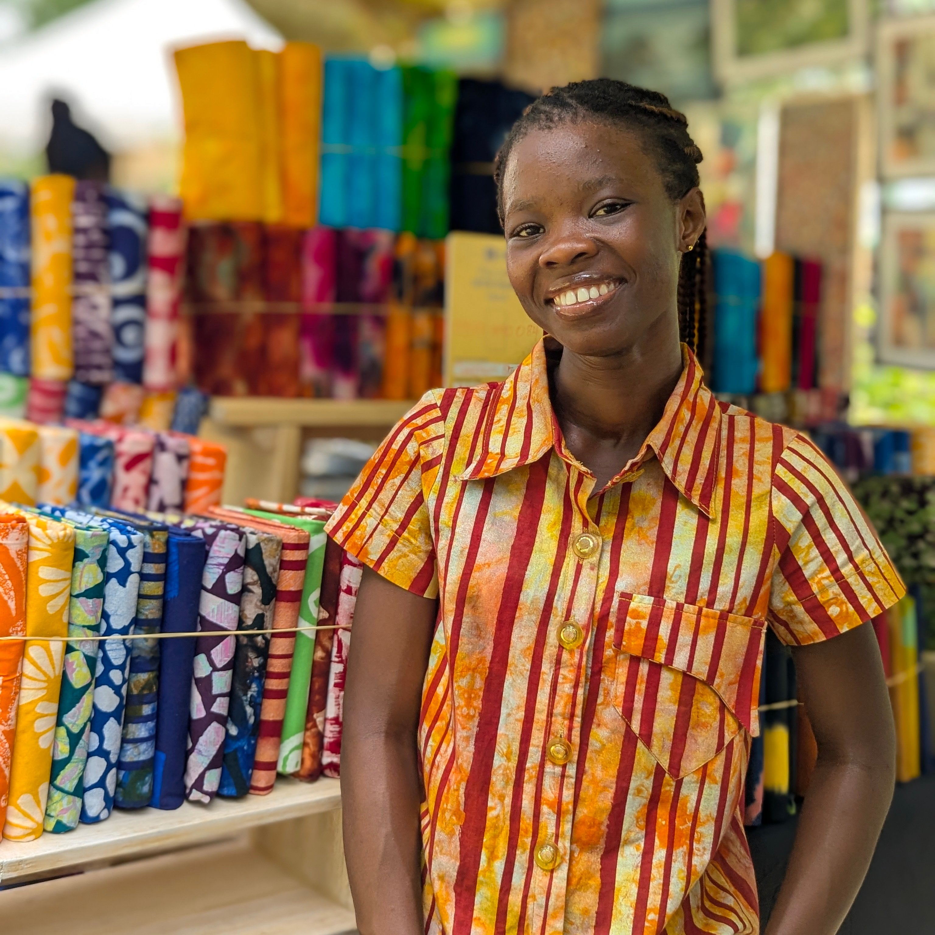 Woman standing in front of a display of colorful fabrics in a store tampoori-batik-shop-labone-accra