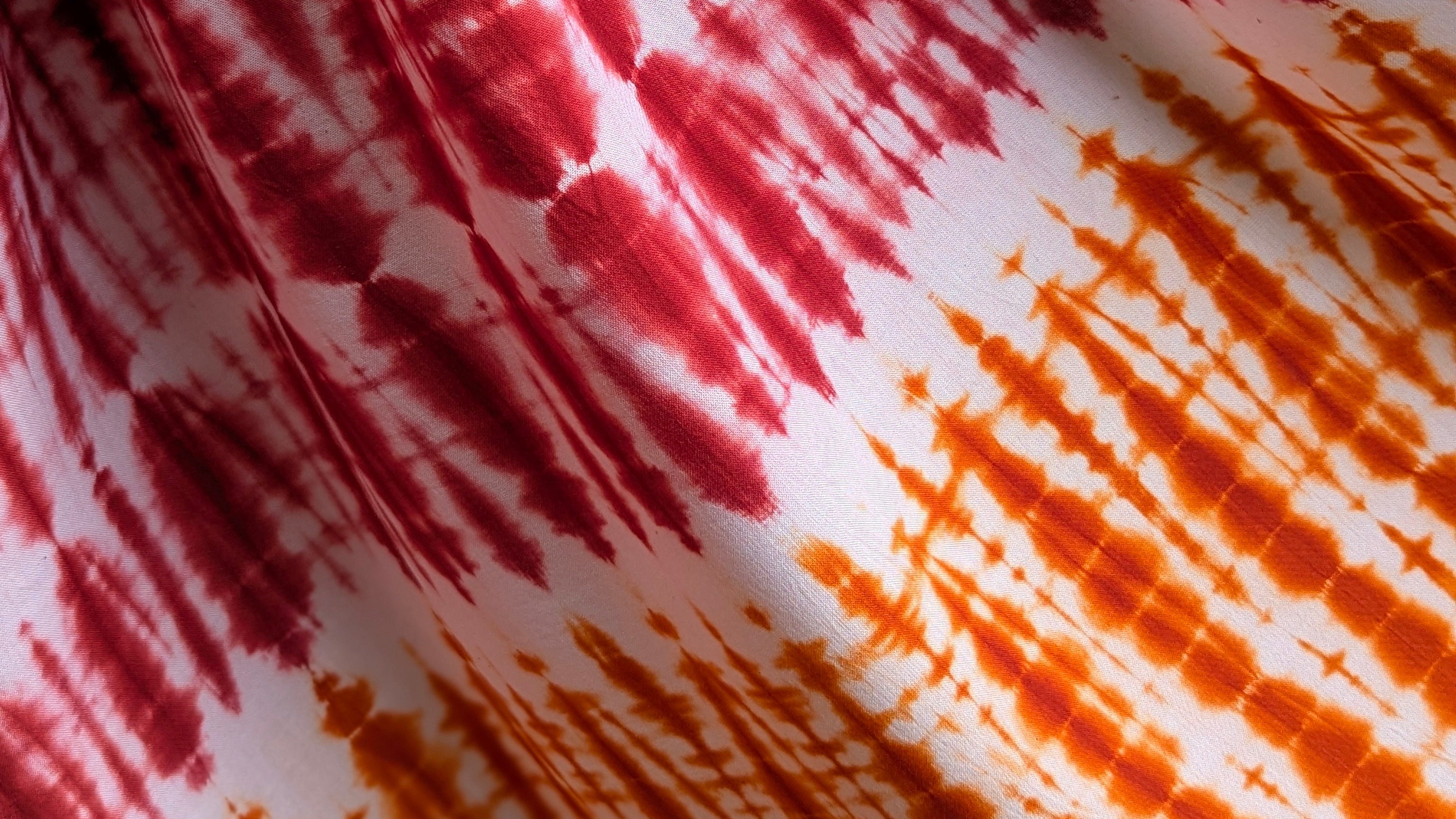 Close-up of fabric with red and orange tie-dye pattern. Custom hand-dyed fabrics created by Tampoori artisans in Accra, Ghana bespoke batik and tie-dye with colour matching textiles for designers and brands, weddings, groups and associations